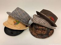 Photo showing all six hats stacked to display variety and colors, including beige, checkered, brown, black hats with feather decorations.
