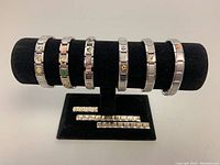 Full view of six stainless steel interlocking link bracelets on a black display stand, including extra links in front.