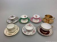 Seven bone china teacups with matching saucers, displaying varied floral patterns and colors including green, pink, gold, and maroon.