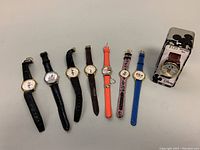 All 8 children's Disney character wristwatches arranged side by side on a flat surface. Varied colors and designs visible.
