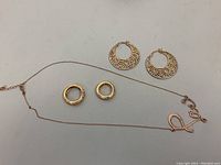 Lot of gold-tone jewelry including a rose-gold tone 'Love' necklace, two gold-tone cubic zirconia rings, and gold-tone hoop earrings.