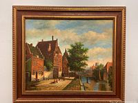 Full view of framed oil painting showing village canal, buildings, people and sky.