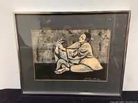 Framed ink and wash painting depicting a mime seated on the floor facing left, framed under glass with a metal frame.