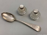 Sterling silver spoon with cut crystal salt and pepper shakers with mother of pearl lids on neutral surface.