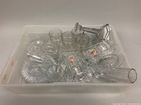 Top view of bin showing assorted clear crystal and glassware including vases, goblets, candleholders, and dishes with some vintage stickers.