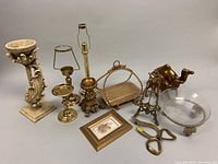 Overview photo of all lot items showing the towel holder, candleholders, basket, camel figurine, glass bowl, hat hook, floral print and scissors.