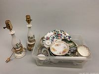 Plastic bin filled with assorted vintage chinaware: floral patterned plates with birds, wildlife scenic plates, multiple small teacups, saucers and small dishes