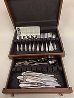 Top drawer of wooden chest open showing 12 teaspoons, 12 luncheon forks, 12 dinner spoons, and 1 serving spoon, arranged in black insert compartments.