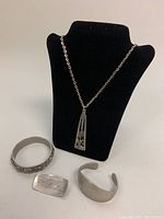 Photo showing necklace displayed on a black stand with pendant, two pewter bangles, and a brooch laid flat on a white background.
