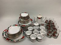 Full view of the complete set including stacked plates, bowls, cups, teapot, and glass tumblers all arranged on a white surface.