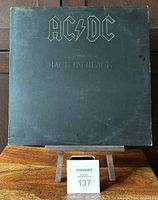 Front cover of AC/DC Back in Black vinyl album showing black cover with embossed band logo and title, displayed on wooden surface.