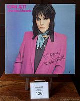 Front cover of Joan Jett & The Blackhearts 'I Love Rock n Roll' album, featuring Joan Jett in a pink blazer and a blue scarf with handwritten 'I love Rock-n-Roll' inscription in black ink.