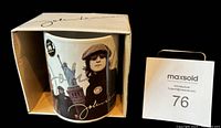 Coffee cup inside original box with visible John Lennon name on flap and cup showing graphics including Statue of Liberty.