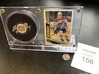 Full display of Lucite case containing Nick Suzuki signed puck and rookie card, quarter for size reference.