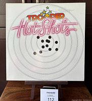 Front cover of the Trooper Hot Shots vinyl LP showing white background with target design and colorful text.