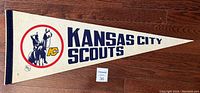 Full view of the triangular Kansas City Scouts NHL felt pennant resting on a wooden floor, showing team name and logo clearly.