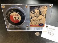Lucite display case containing a signed hockey puck and signed hockey card by Yvon Cournoyer. Includes a coin for scale and auction lot number.