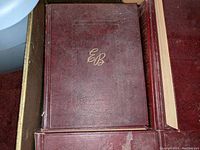 Close-up photo of a single volume from the Encyclopedia Britannica 1954 24-volume set featuring the dark red leather hard cover with gold embossed EB letters.