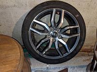Photo shows one Scion tC alloy rim with original tire mounted, the rim features a multi-spoke black and silver design with a Scion logo center cap.