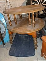 2-tier round wooden table with turned legs and natural finish shown from side angle
