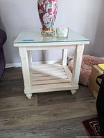 Front-left angle showing distressed wood finish, glass top, and slatted bottom shelf with rounded legs.