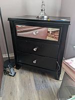 Front view of the black faux leather and wood end table with mirror drawer and crystal knobs, showing scratches and overall condition.
