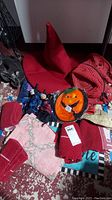 Photo of red pointed witch hat, red towels, a round pumpkin hanging decor, and multiple Halloween related items on a red patterned carpet.