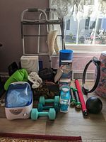 Wide view of the healthcare and exercise lot showing walker, neck pillows, weights, medicine ball, and other items