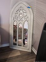 Full view of archway style mirror leaning against a wall, showing the three vertical mirror panels and decorative cut-out frame.
