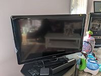 Front view of the black Philips 40 inch TV on its stand with remote and some items nearby.