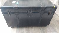 Front view of black leatherette trunk showing metal straps and latches with some surface wear