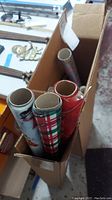 Two boxes filled with several rolls of assorted holiday-themed wrapping paper, including plaid and snowman patterns, viewed from above.