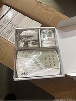 Photo showing an open box with one complete Orbic alarm system including main control panel with keypad, motion sensor, and accessories.