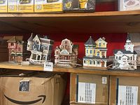 Five miniature buildings on a shelf including Victorian and lighthouse style detailed holiday houses with electric cord and roller switch