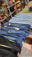 Lot of jeans folded and laid out showing various styles and washes, mostly blue denim.