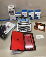 Overview photo showing Brother label printer, four new label cassettes, red BOVIS phone case in package, and Merece weather station components with manual.