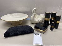 View of all items on table: three Chanel cologne bottles, one loose bath powder container, Lenox swan figurine with dish, black clutch purse.