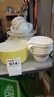 Stack of white Corelle cups and bowls with golden floral pattern, and yellow Pyrex mixing bowl.