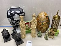 Group photo showing all main decorative items in lot including large black and egg-shaped vases, two carved figurines, brass lattice tower, pair of dark stone lions, and small carved animal figures.