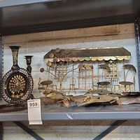 Shelved display of multiple black and gold metal decorative items including wall hangings and sculptures.