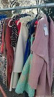 Various dresses and coats hanging on a rack, different colors and patterns including animal print, cream, pink, blue and mint green lace dress visible