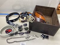 Overview showing multiple belts, belt buckles, sunglasses, and silver chain with lion head charm