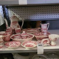 Full view of porcelain china pieces on shelf showing varied items including coffee pot, jugs, plates, cups, bowls in red transferware design