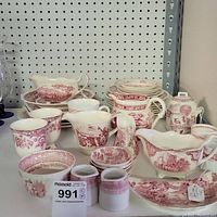 Group shot of red and white porcelain china collection arranged on table with various plates, cups, gravy boats, and small pitchers, showing the full set and detailed red scenic patterns.