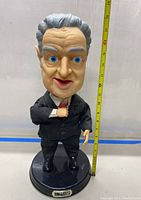 Full front view of the approximately 19-inch tall Rodney Dangerfield talking doll standing on a flat surface next to a measuring tape showing its height.
