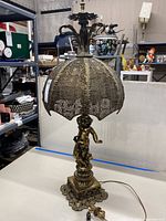 Full view of tall metal cherub lamp showing the base, cherub figure, and pierced metal shade.
