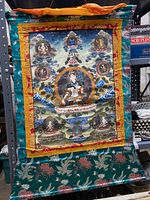 Full view of painted Tibetan thangka with brocade border hung on shelf