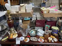 Full view of various vintage items on metal shelving including lamp, decanters, boxes, crystals, pins.
