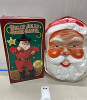 Holly Jolly Rock Santa figurine in box with large plastic Santa face door hanging side by side