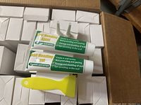 Box containing multiple white boxes, each containing a new tube of Wall Mending Agent Spackle and a yellow plastic scraper tool. Two tubes and one scraper visible on top.